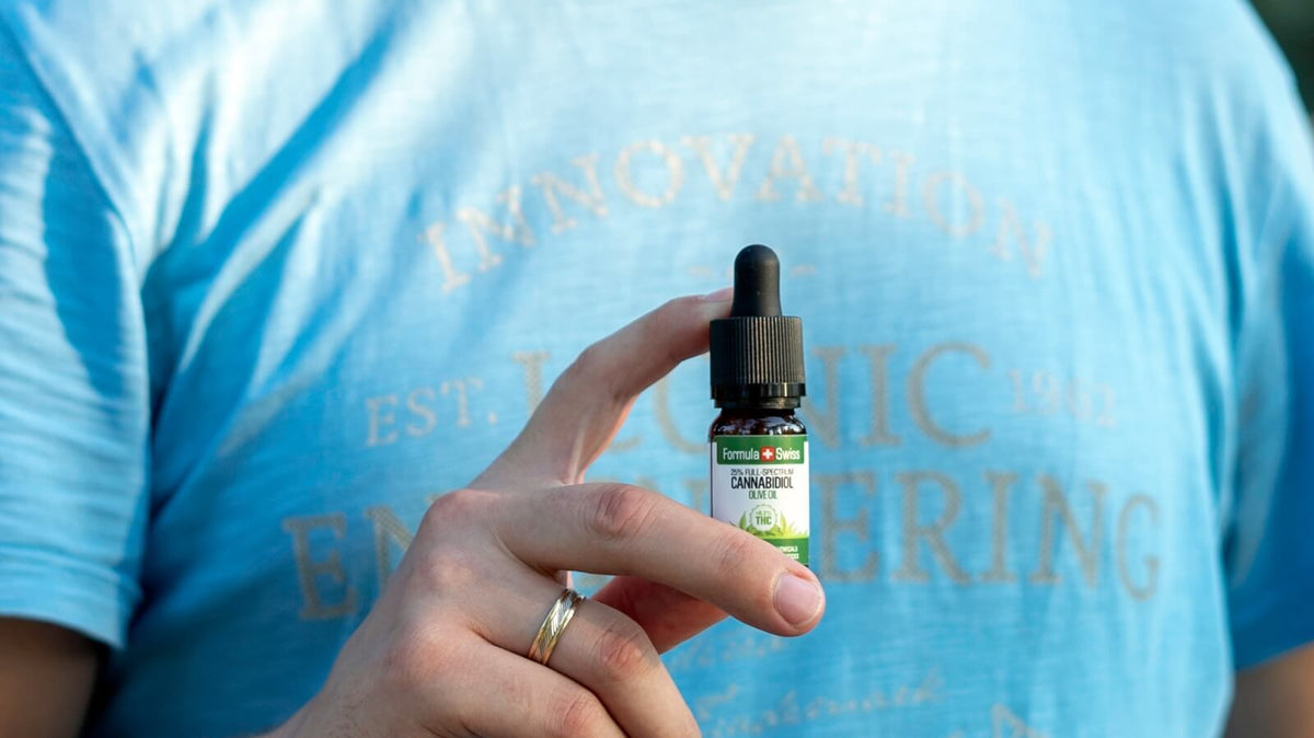 Close-up of a hand holding a bottle of Formula Swiss CBD oil in olive oil against a blue T-shirt